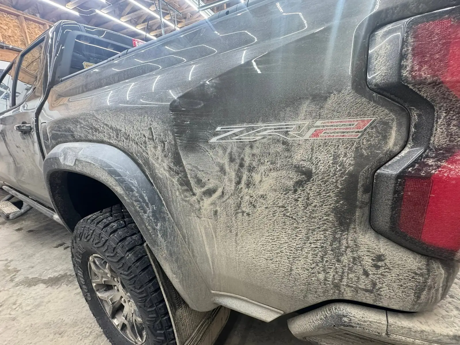 Chevy Colorado ZR2 caked in mud along the rear door and bed, before
